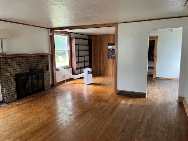 unfurnished living room featuring hardwood / wood-style floors, wooden walls, a brick fireplace, and a textured ceiling