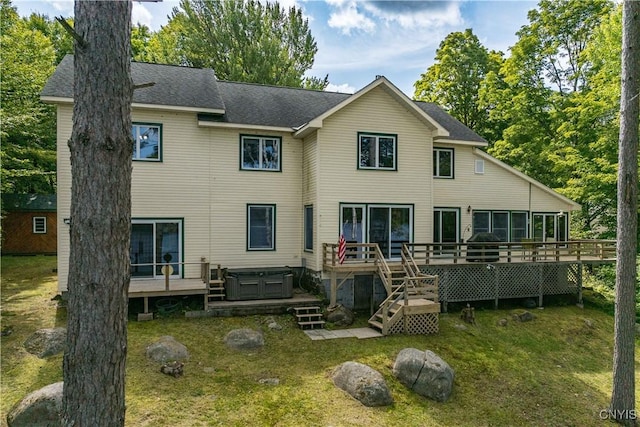 back of property with a deck, a shingled roof, a lawn, and a hot tub