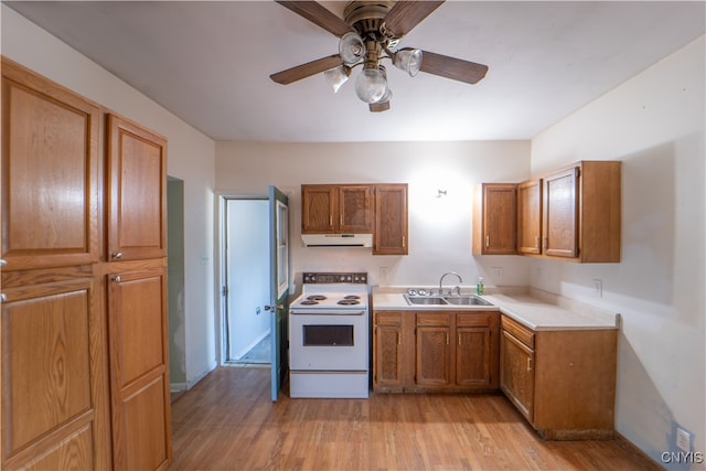 kitchen with under cabinet range hood, a sink, electric stove, light countertops, and brown cabinets