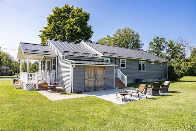 rear view of house featuring an outdoor fire pit, metal roof, an outbuilding, a yard, and a patio area