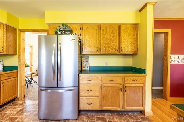 kitchen featuring brown cabinetry, freestanding refrigerator, and baseboards