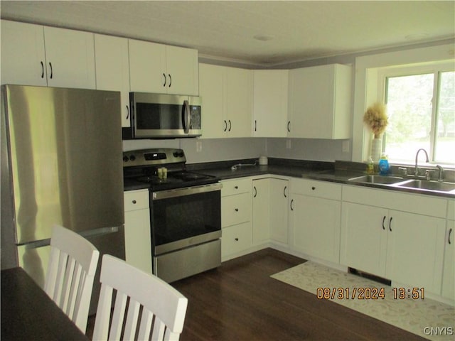 kitchen with white cabinetry, a sink, dark countertops, dark wood-style floors, and appliances with stainless steel finishes