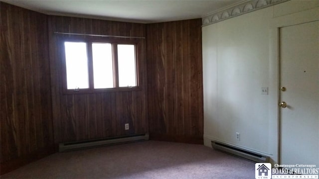 carpeted spare room with a baseboard heating unit and wooden walls