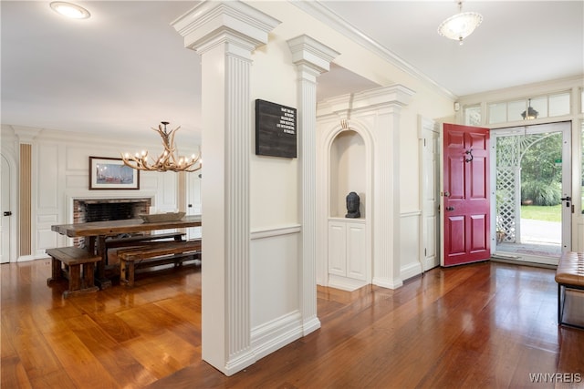 entryway featuring crown molding, dark hardwood / wood-style floors, decorative columns, and a notable chandelier