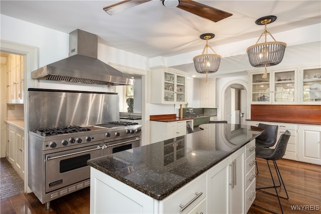 kitchen with double oven range, a kitchen island, ceiling fan, white cabinets, and wall chimney range hood