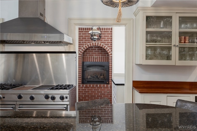 kitchen with high end stove, a fireplace, wall chimney exhaust hood, and dark stone counters