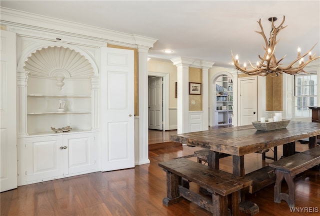 dining space featuring an inviting chandelier, decorative columns, built in shelves, crown molding, and dark wood-type flooring