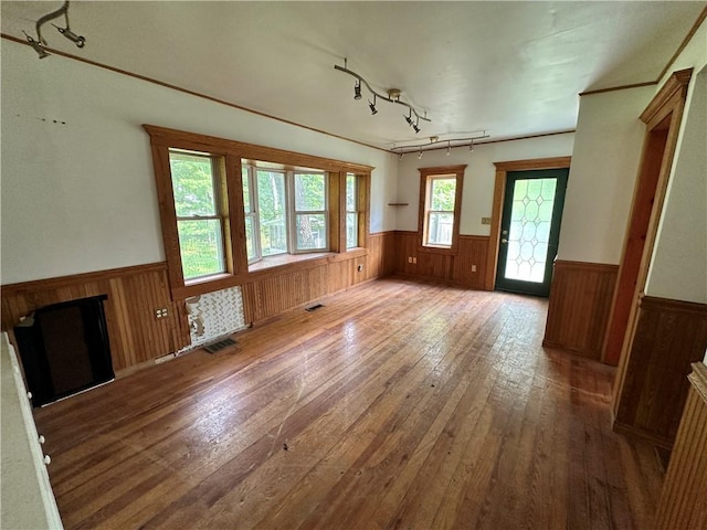 unfurnished living room with wooden walls, a wainscoted wall, visible vents, hardwood / wood-style floors, and rail lighting