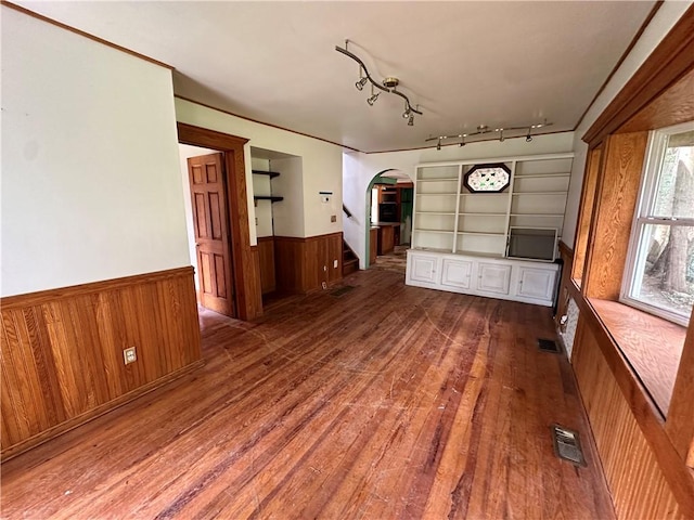 unfurnished living room with arched walkways, a wainscoted wall, visible vents, stairs, and wood-type flooring