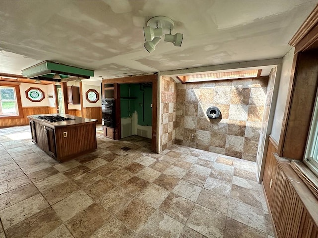 kitchen with a center island, a wainscoted wall, gas stovetop, radiator, and wood walls