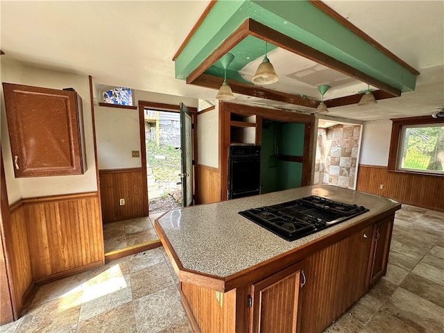 kitchen featuring black appliances, wooden walls, stone tile flooring, and wainscoting