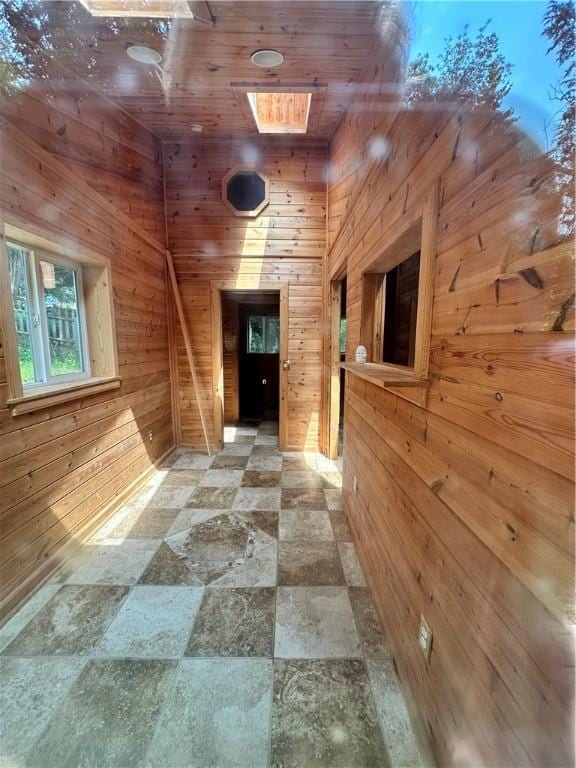 corridor featuring a skylight, wooden ceiling, and wooden walls