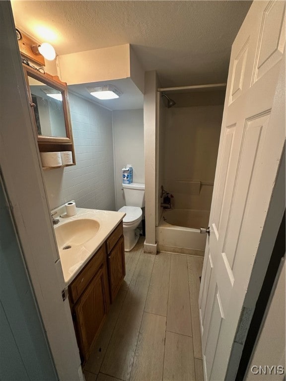 full bathroom featuring a textured ceiling, vanity, toilet, and tiled shower / bath