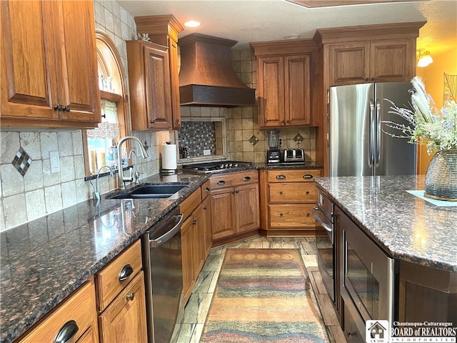 kitchen featuring sink, appliances with stainless steel finishes, custom range hood, and dark stone counters