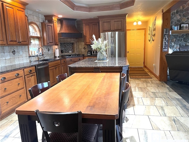 kitchen featuring premium range hood, sink, a kitchen island, a stone fireplace, and appliances with stainless steel finishes