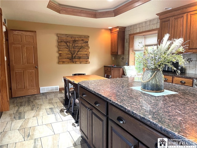 kitchen with decorative backsplash, dark stone countertops, and a tray ceiling