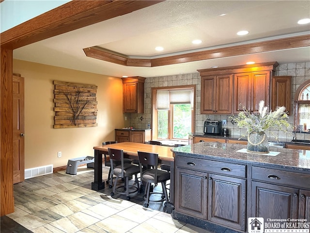 kitchen featuring crown molding, dark stone countertops, a tray ceiling, and tasteful backsplash