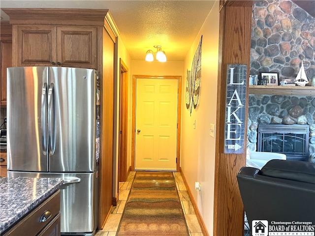 kitchen featuring stainless steel fridge, a fireplace, a textured ceiling, dark stone counters, and tile patterned floors