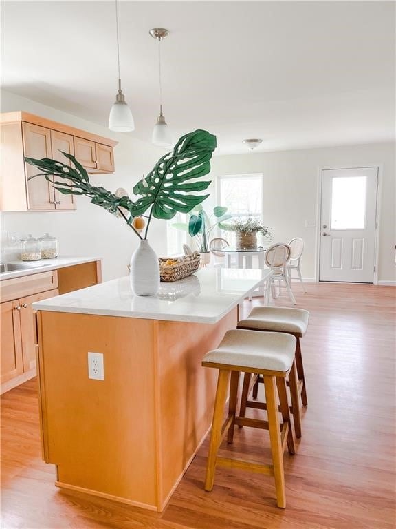 kitchen featuring light brown cabinets, a kitchen island, decorative light fixtures, a kitchen breakfast bar, and light wood-type flooring