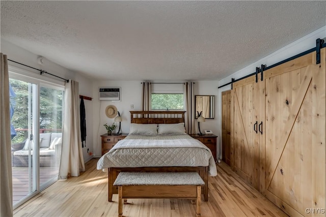 bedroom featuring light wood finished floors, a barn door, access to outside, and a wall mounted AC