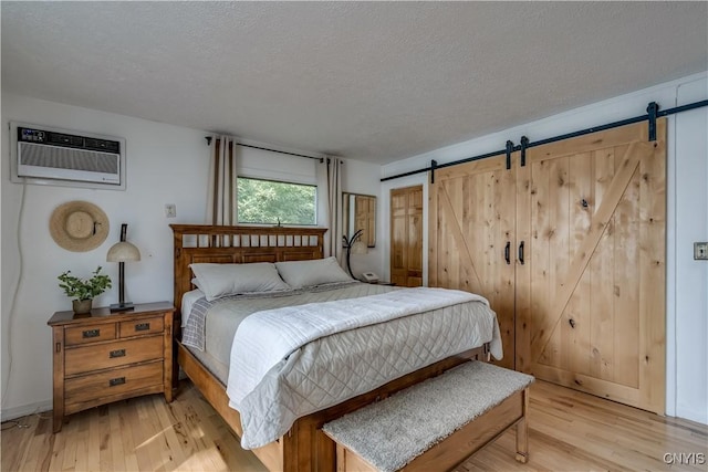 bedroom with light wood finished floors, a barn door, a textured ceiling, and an AC wall unit