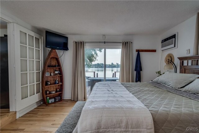 bedroom with a textured ceiling, an AC wall unit, access to outside, and light hardwood / wood-style floors