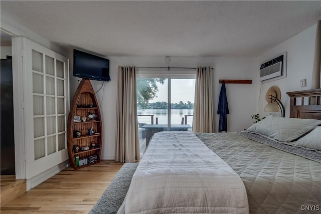 bedroom featuring a textured ceiling, access to outside, an AC wall unit, and wood finished floors