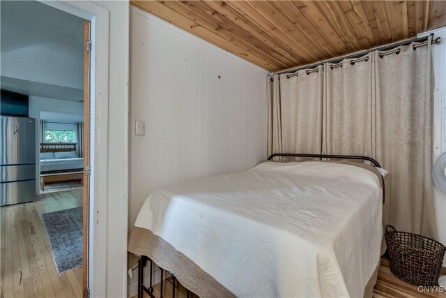 bedroom featuring vaulted ceiling, light hardwood / wood-style floors, stainless steel refrigerator, and wooden ceiling