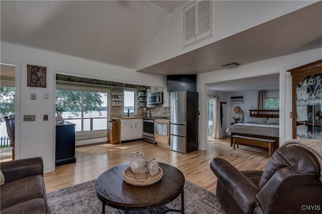 living area featuring a wall unit AC, visible vents, light wood-style flooring, a baseboard heating unit, and high vaulted ceiling