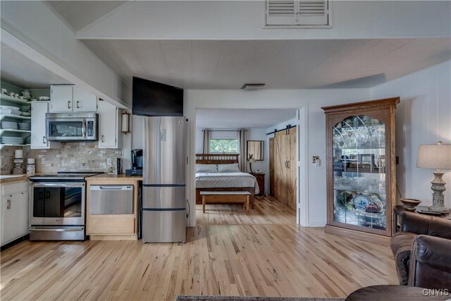 kitchen featuring a barn door, light wood-type flooring, appliances with stainless steel finishes, and white cabinetry