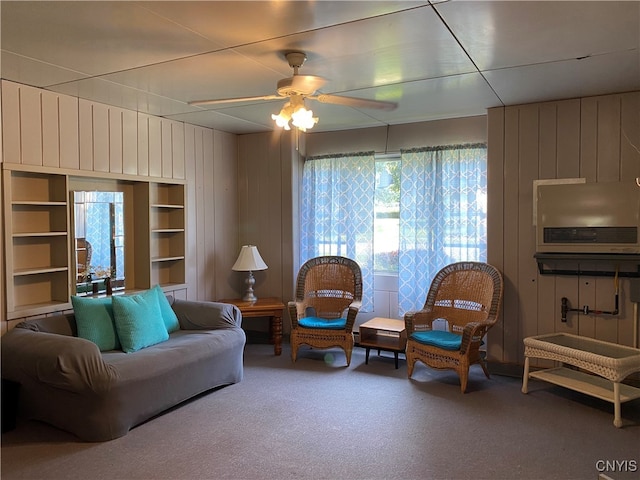 carpeted living room featuring wood walls, ceiling fan, and a healthy amount of sunlight