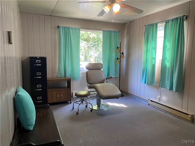 living area featuring a baseboard heating unit, dark carpet, ceiling fan, and wooden walls