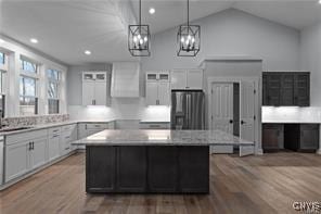 kitchen featuring light countertops, stainless steel fridge, decorative light fixtures, a kitchen island, and wood finished floors