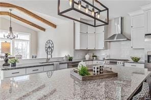 kitchen featuring white cabinetry, an inviting chandelier, hanging light fixtures, vaulted ceiling with beams, and wall chimney exhaust hood