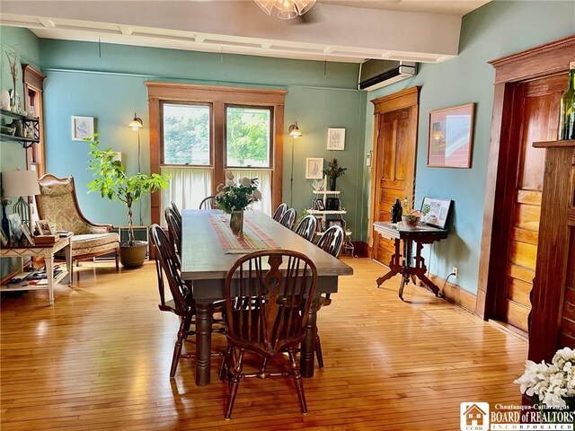 dining area with beam ceiling, a wall mounted AC, and light hardwood / wood-style flooring