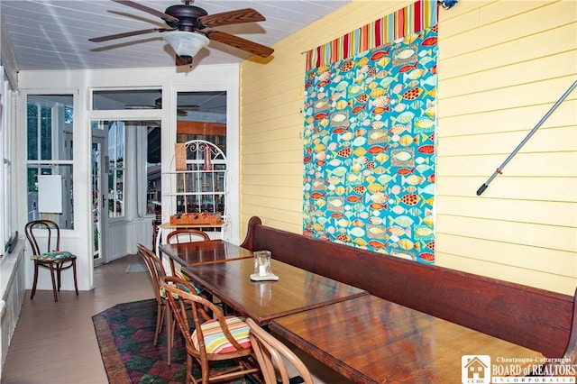 dining area with ceiling fan and wooden walls