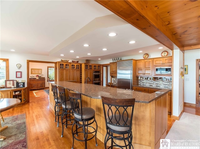 kitchen with light hardwood / wood-style flooring, a large island, built in appliances, tasteful backsplash, and a breakfast bar