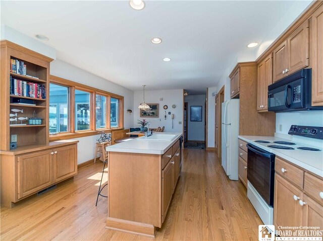 kitchen with white appliances, a center island with sink, light hardwood / wood-style floors, hanging light fixtures, and a breakfast bar