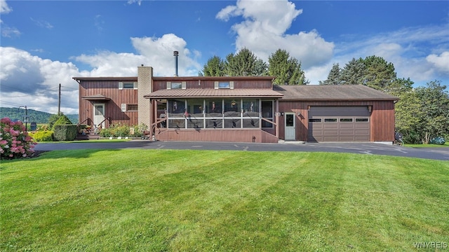 rear view of property featuring a lawn, a garage, and a sunroom