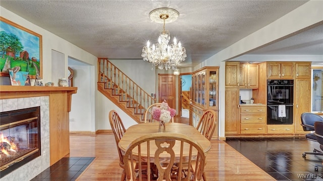 dining space with a textured ceiling, a tiled fireplace, dark hardwood / wood-style floors, and a notable chandelier