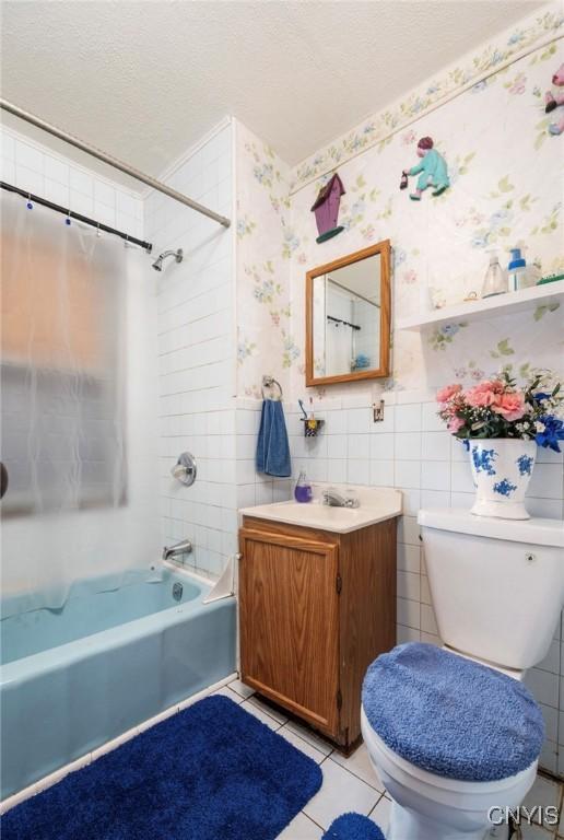 full bathroom with tile patterned floors, toilet, shower / tub combo with curtain, vanity, and a textured ceiling