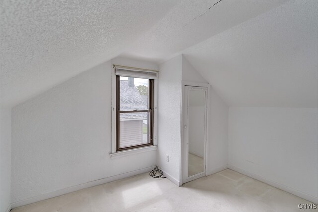 bonus room featuring lofted ceiling, light colored carpet, and a textured ceiling