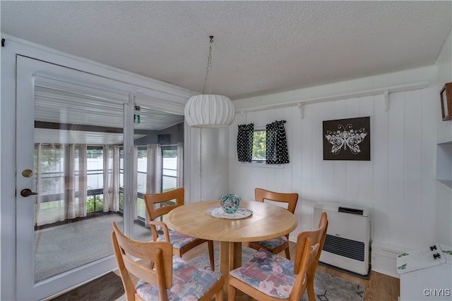 dining room with a textured ceiling, hardwood / wood-style flooring, heating unit, and wood walls