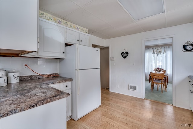 kitchen featuring backsplash, light wood-type flooring, a notable chandelier, white cabinetry, and white fridge