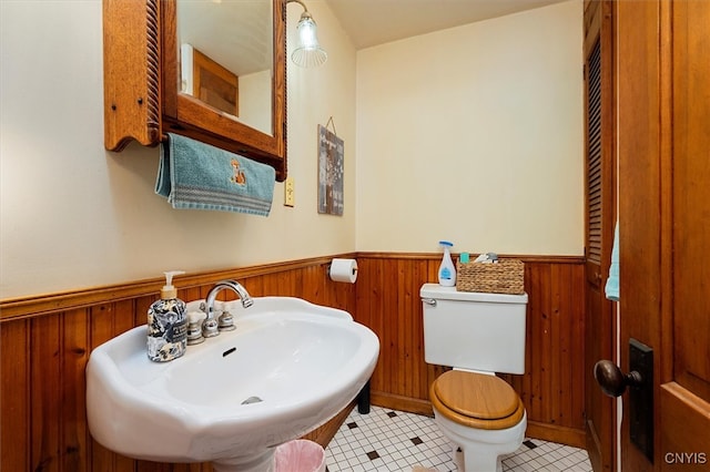 bathroom with toilet, wood walls, sink, and tile patterned floors