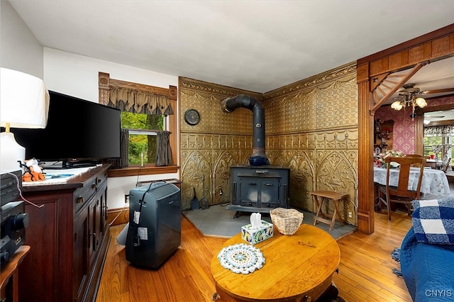 living room with ceiling fan, a wood stove, and light hardwood / wood-style floors