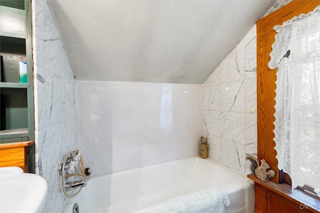 bathroom featuring vaulted ceiling, a textured ceiling, and bathtub / shower combination