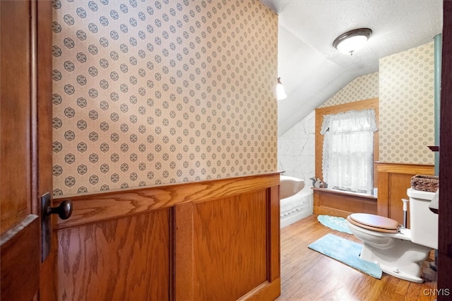 bathroom featuring hardwood / wood-style flooring, toilet, a tub, lofted ceiling, and a textured ceiling