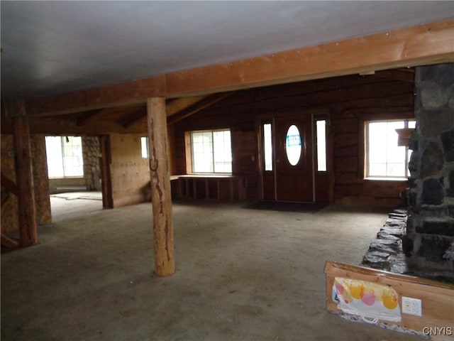 foyer entrance featuring log walls, a stone fireplace, carpet floors, and vaulted ceiling with beams