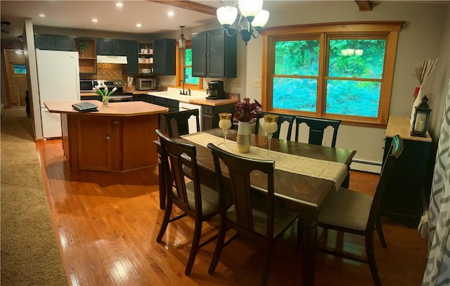 dining room with sink, light wood-type flooring, a baseboard heating unit, and a notable chandelier